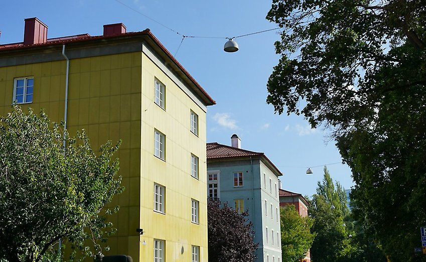 Fasaden på ett gult flerfamiljshus i solsken.